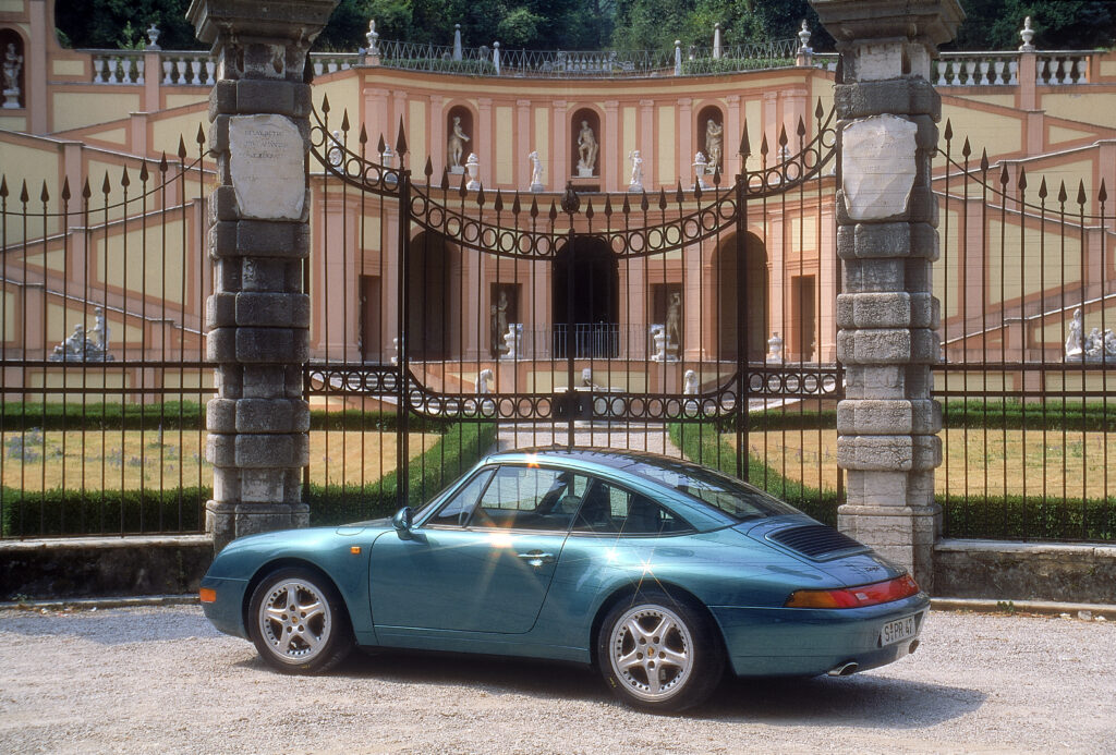 1997 Porsche 911 Targa sitting in front of a locked gate with an antique European building as the backdrop