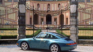 1997 Porsche 911 Targa sitting in front of a locked gate with an antique European building as the backdrop