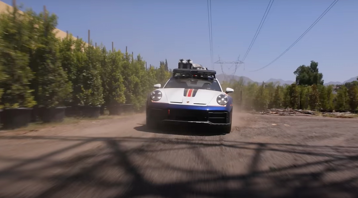 A Porsche 911 Dakar kicks up dirt with Jay Leno. 